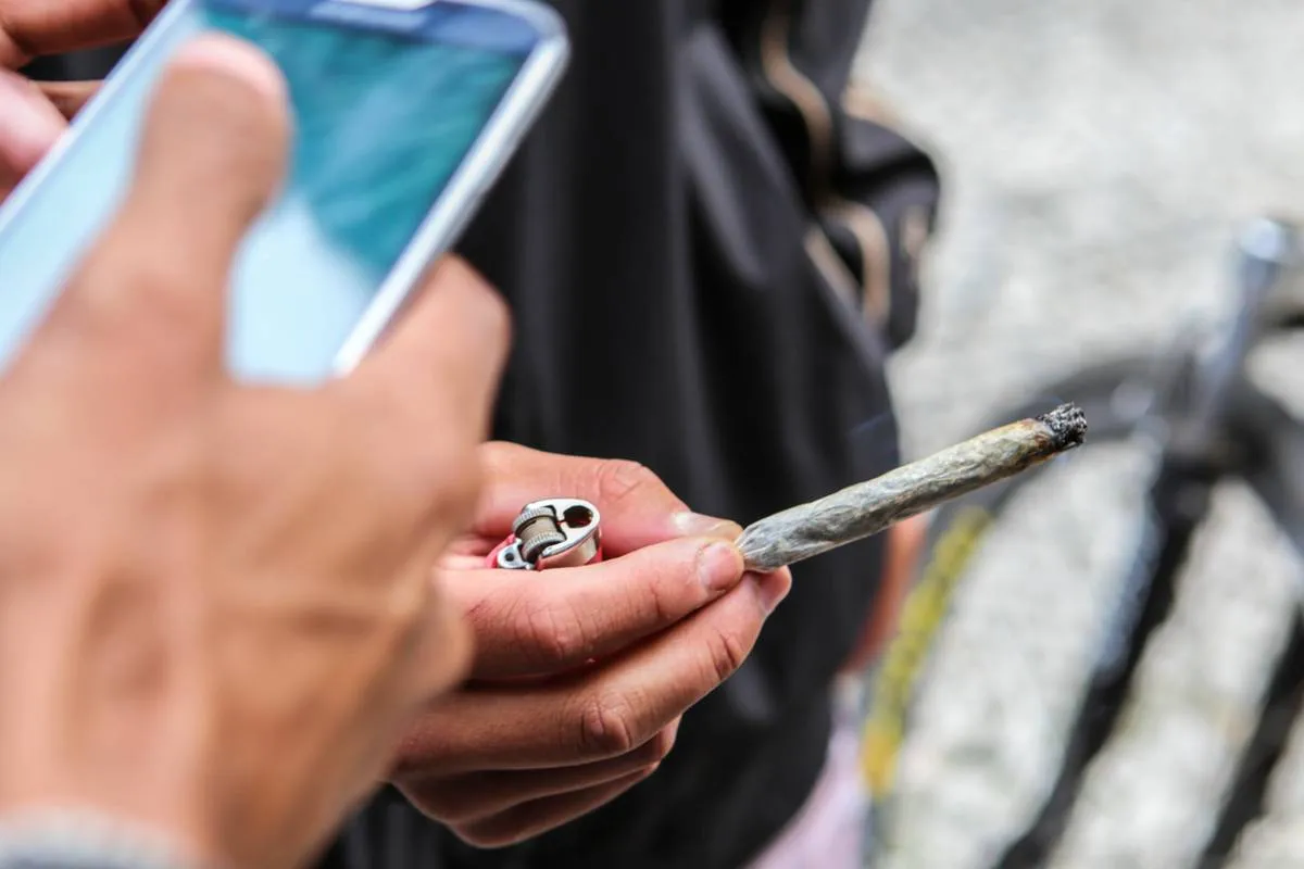 Imagem mostra uma pessoa segurando um cigarro de maconha