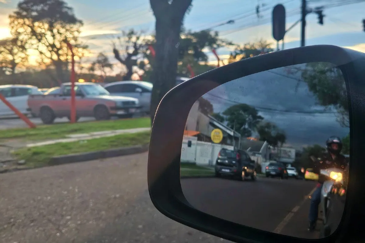 Imagem mostra o céu em Curitiba com um pouco de sol e, no retrovisor do carro, a imagem do céu super fechado e carrancudo.