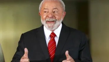 Imagem mostra Lula, presidente do Brasil, com uma gravaata vermelha rindo e "joinha" com as duas mãos
