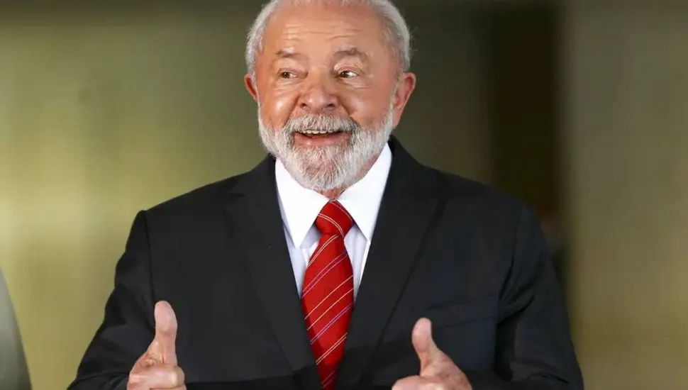 Imagem mostra Lula, presidente do Brasil, com uma gravaata vermelha rindo e "joinha" com as duas mãos