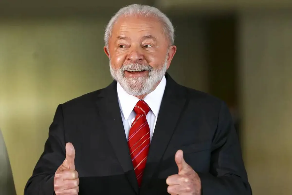 Imagem mostra Lula, presidente do Brasil, com uma gravaata vermelha rindo e "joinha" com as duas mãos