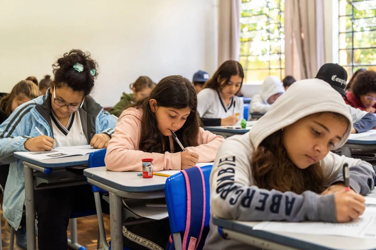 Imagem mostra estudantes em um colégio público do Paraná. Eles estão agasalhados e fazendo uma prova.