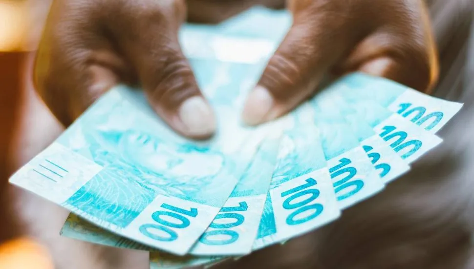 Imagem mostra uma pessoa segurando 7 notas de 100 reais.