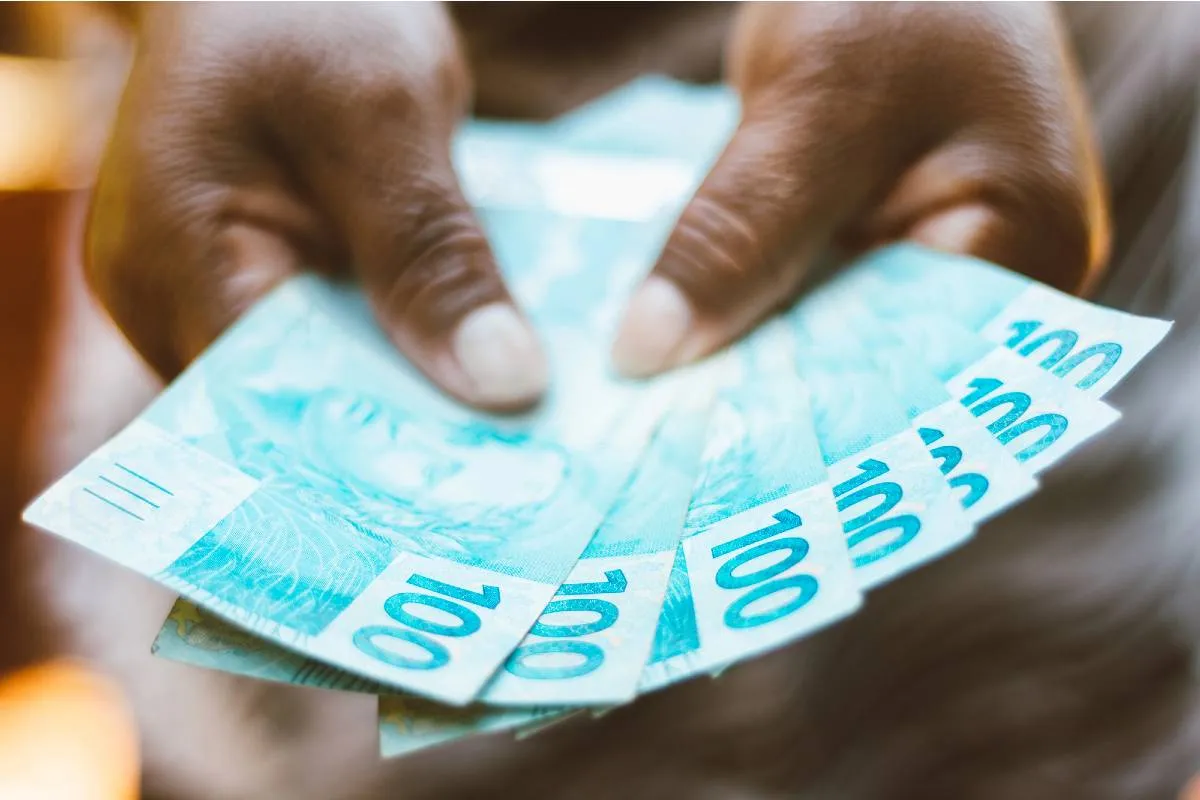 Imagem mostra uma pessoa segurando 7 notas de 100 reais.