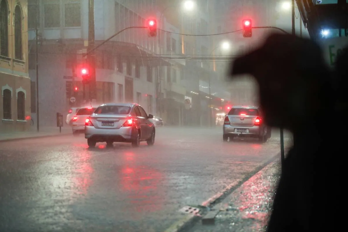 Imagem mostra um temporal em Curitiba, com carros parando num sinal vermelho e muita água pingando no asfalto. No lado direito, a silhueta de um homem de boné.