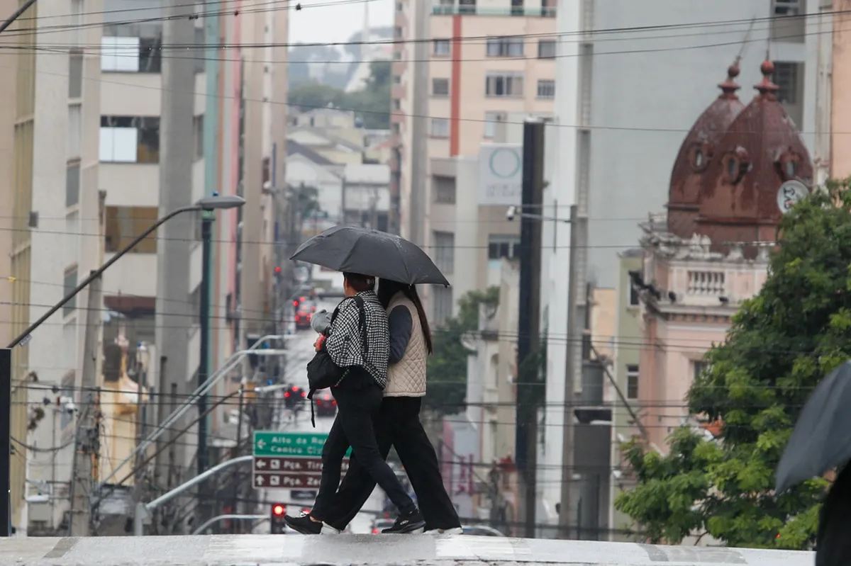 Imagem mostra mulheres andando na rua, usando guarda-chuva em Curitiba