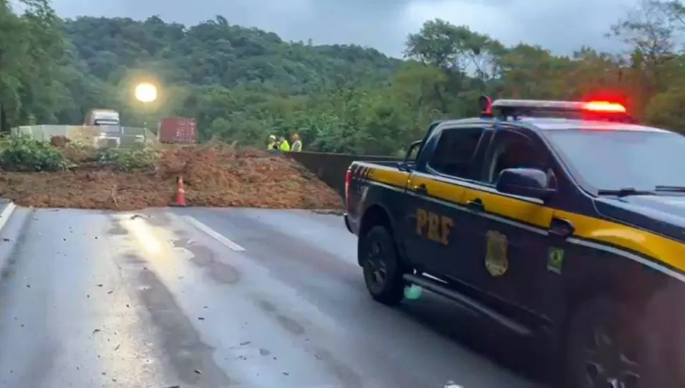 Imagem mostra a rodovia interditada por um deslizamento de terra e uma viatura da PRF.