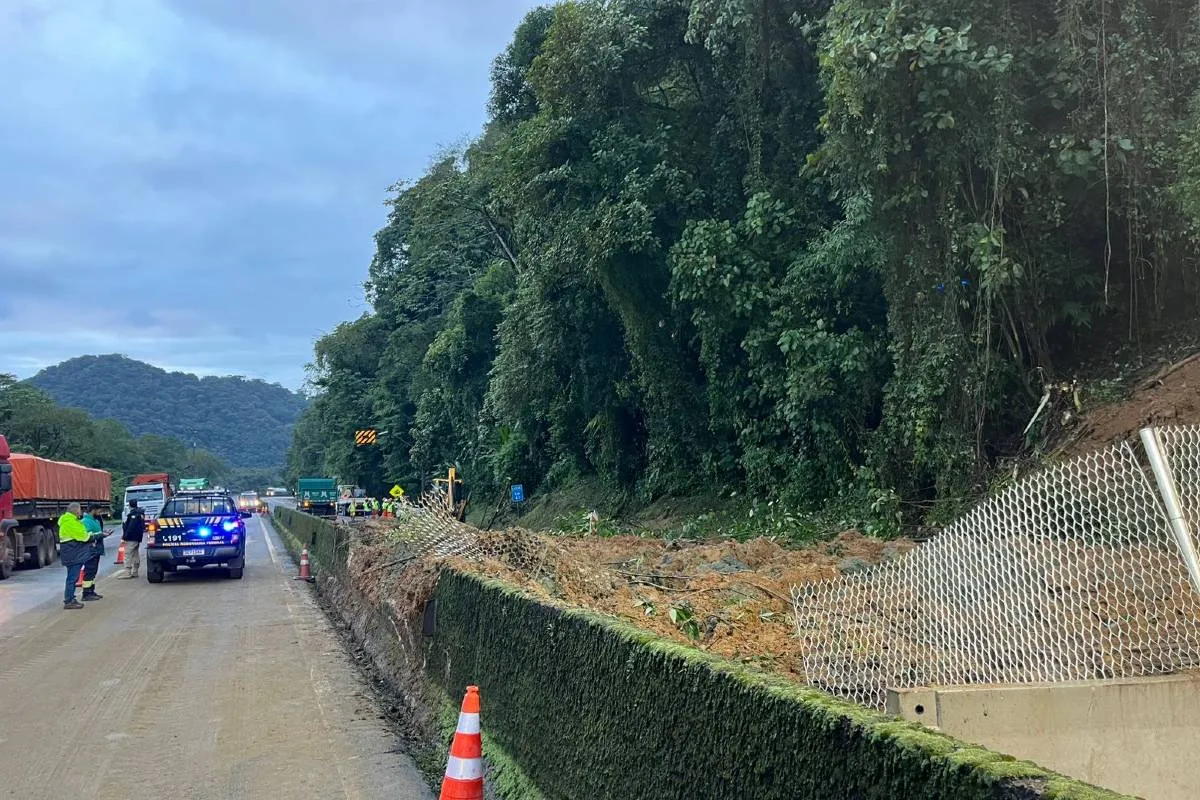 Imagem mostra a rodovia interditada por um deslizamento de terra e uma viatura da PRF.