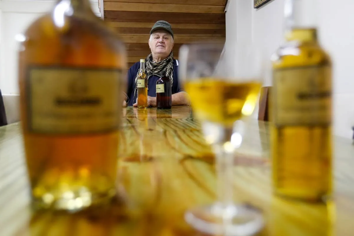 Imagem mostra uma garrafa e uma taça servida com cachaça de cataia. Ao fundo está o criador.