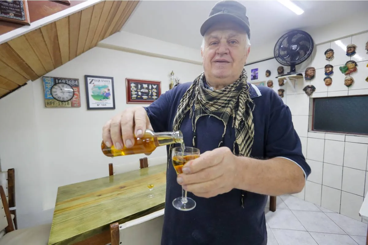 Imagem mostra um homem segurando uma taça e servindo cachaça.
