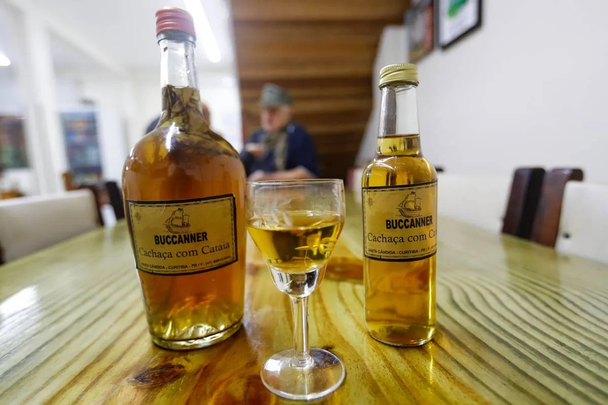 Imagem mostra uma garrafa e uma taça servida com cachaça de cataia.