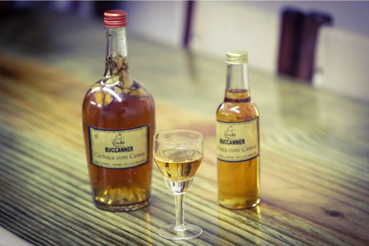 Imagem mostra uma garrafa e uma taça servida com cachaça de cataia.
