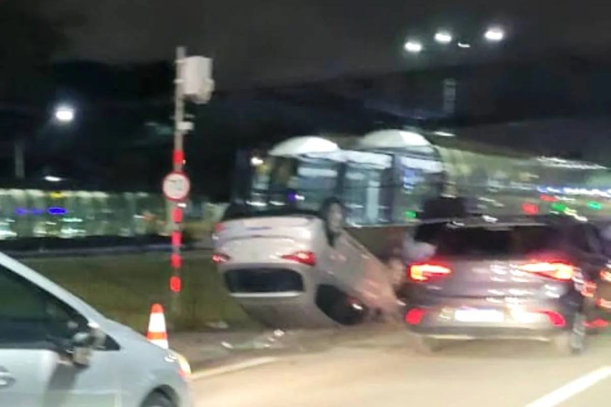 Imagem mostra um carro prateado capotado em uma via de Curitiba.