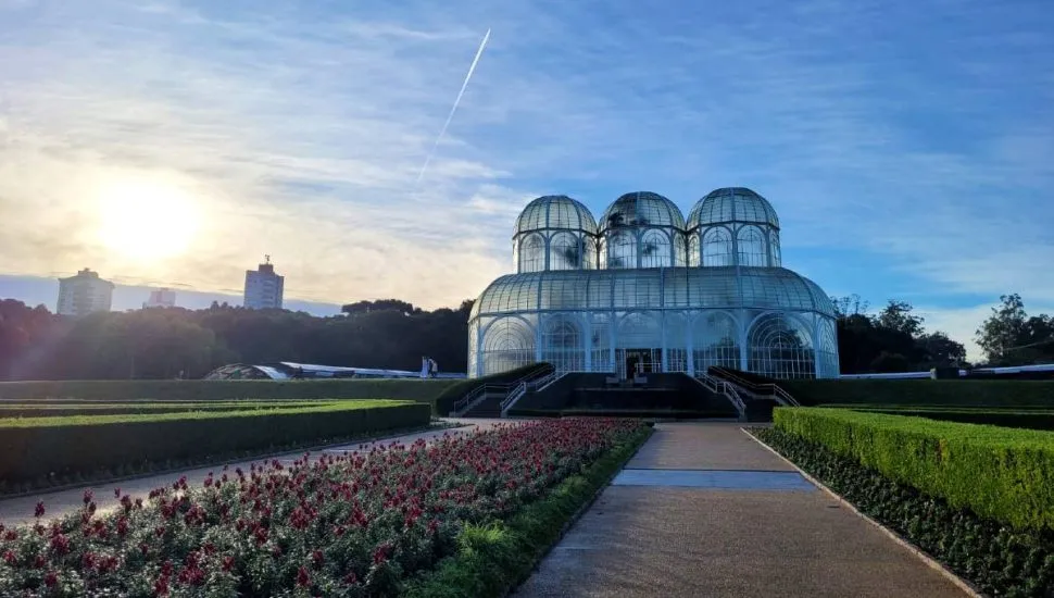 Imagem mostra o Jardim Botânico, em Curitiba, em um dia de muito frio. Céu com poucas nuvens e sol ao lado da famosa estufa.
