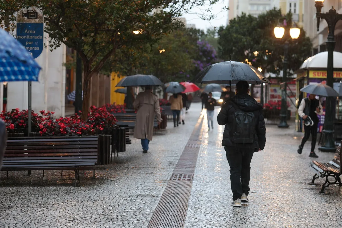 Imagem mostra pessoas com guarda-chuva andando no Centro de Curitiba em dia de chuva