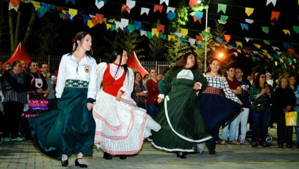 Imagem mostra uma clássica festa junina de igreja com mulheres de vestido dançando debaixo de bandeirinhas.