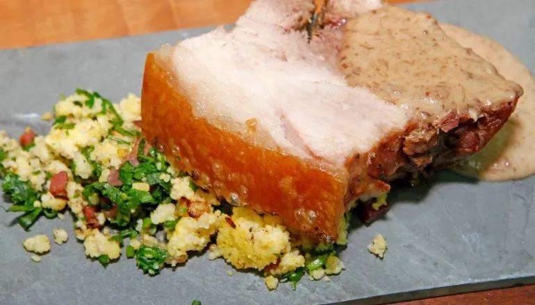 Imagem mostra uma fatia de um porco no rolete com farofinha e molho.