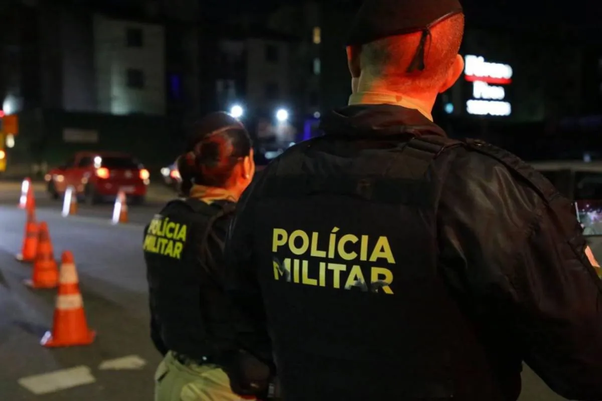 Imagem mostra depois policiais militares de costas m uma rua à noite.