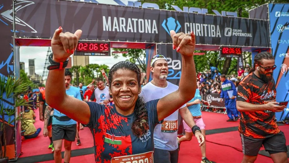 Foto mostra linha de chegada da Maratona de Curitiba, com vários atletas chegando ao térmnao da prova, com destque para uma mulhar com os dois braços erguidos em comemoração ao feito