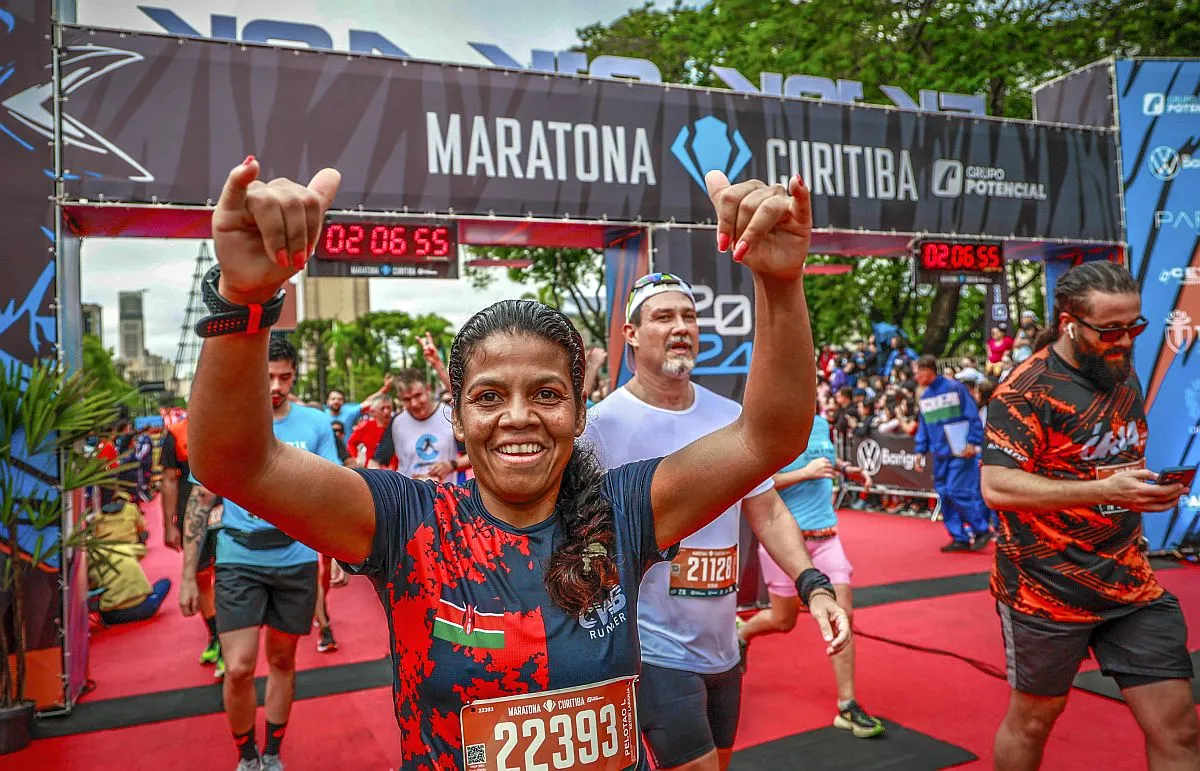 Foto mostra linha de chegada da Maratona de Curitiba, com vários atletas chegando ao térmnao da prova, com destque para uma mulhar com os dois braços erguidos em comemoração ao feito