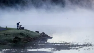 Imagem mostra um lago com fumaça e muito frio. Uma pessoa está na beira olhando