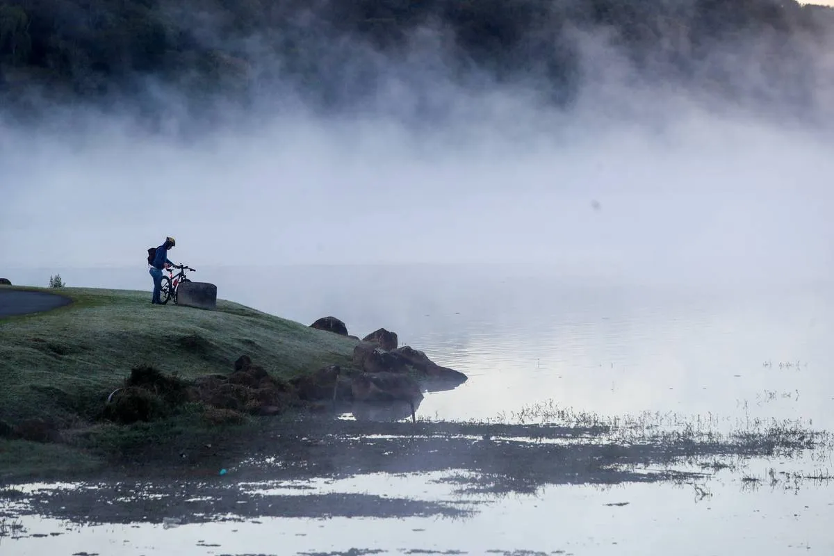 Imagem mostra um lago com fumaça e muito frio. Uma pessoa está na beira olhando