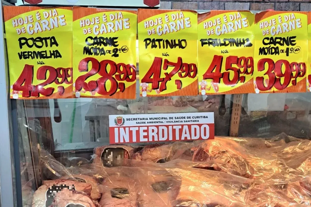 Imagem mostra balcão frigorífico com dezenas de peças de carne, com placas amarelas e os preços e nome de cada corte. No centro, uma faixa escrito INTERDITADO