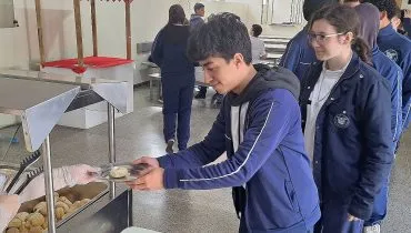 Alunos com o uniforme fazem fila para receber pão de queijo