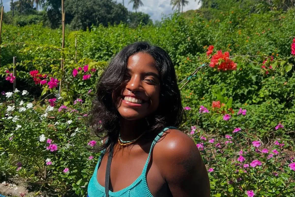 imagem mostra a Juliana Marins em um campo florido com um sorriso