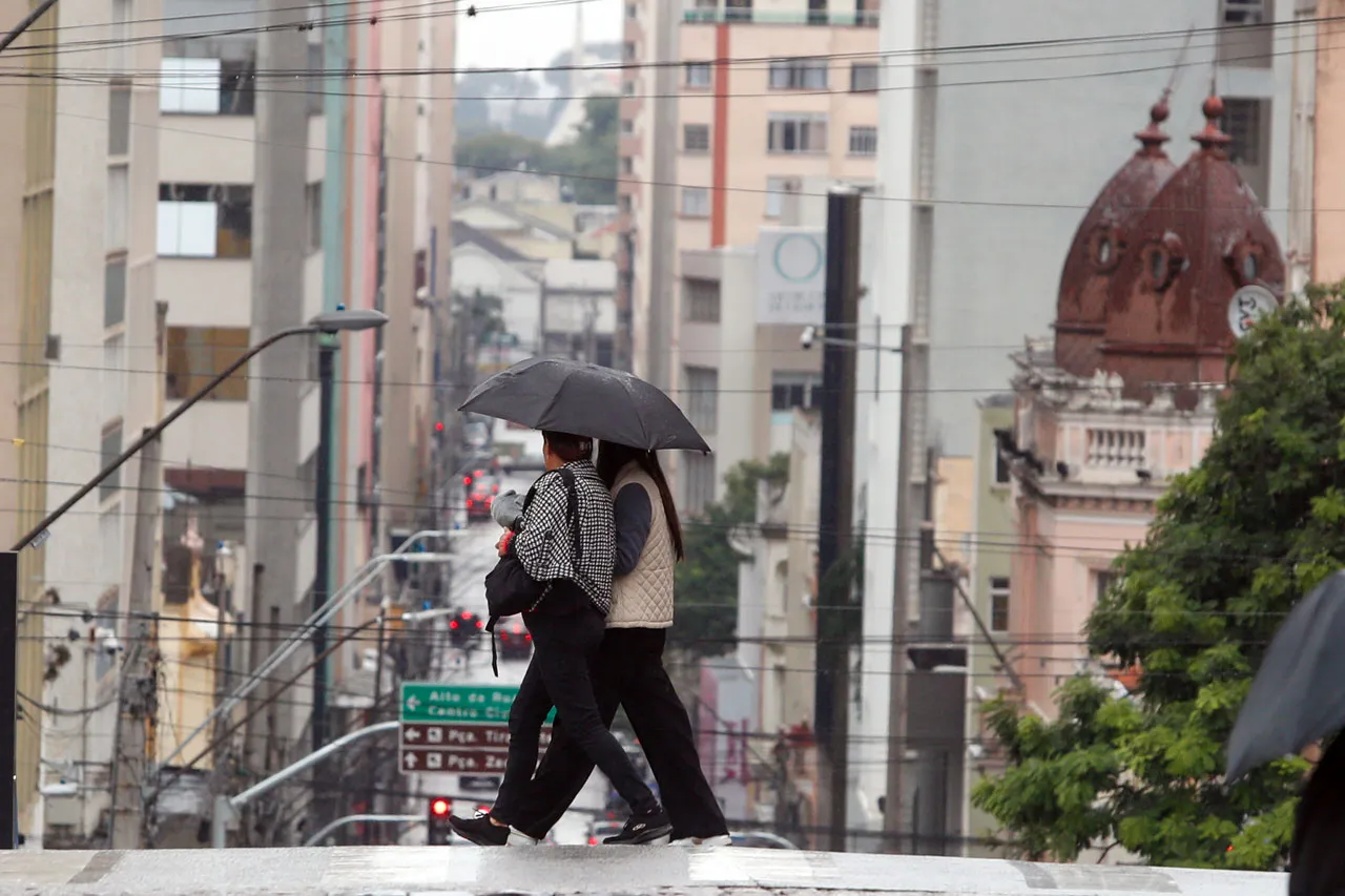 Pessoas caminham na chuva com guarda-chuvas. Há alerta de chuva intensa no Paraná.