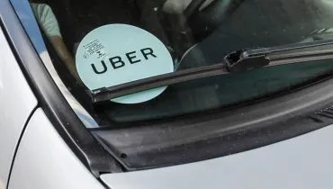 Imagem mostra um carro prata com um adesivo de Uber colado no vidro da frente.