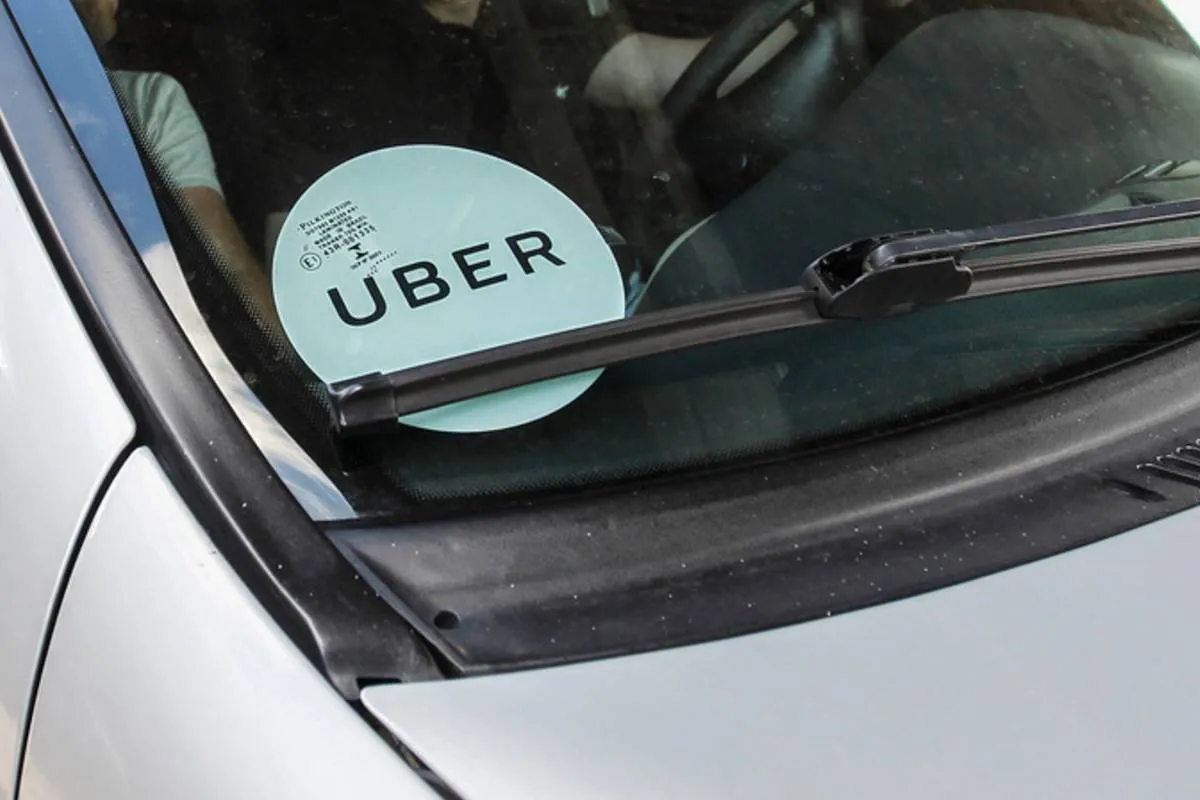 Imagem mostra um carro prata com um adesivo de Uber colado no vidro da frente.
