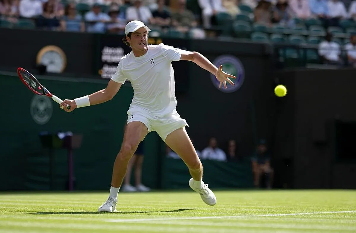 João fonseca em ação, se posiciona para acertar uma raquetada na bolinha, no gramado de Wimbledon