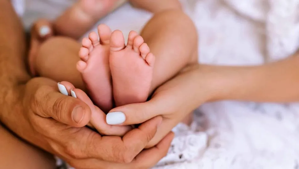 Imagem mostra os pais segurando os pés de um bebezinho recém nascido.