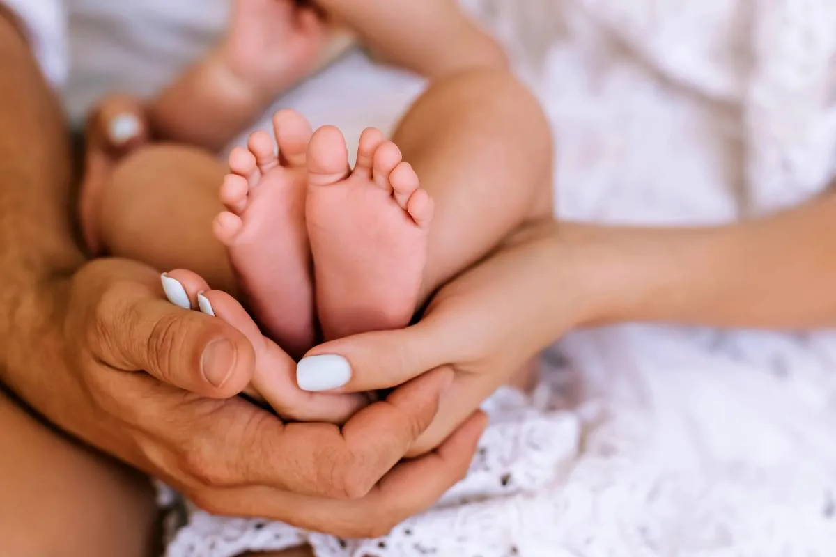 Imagem mostra os pais segurando os pés de um bebezinho recém nascido.