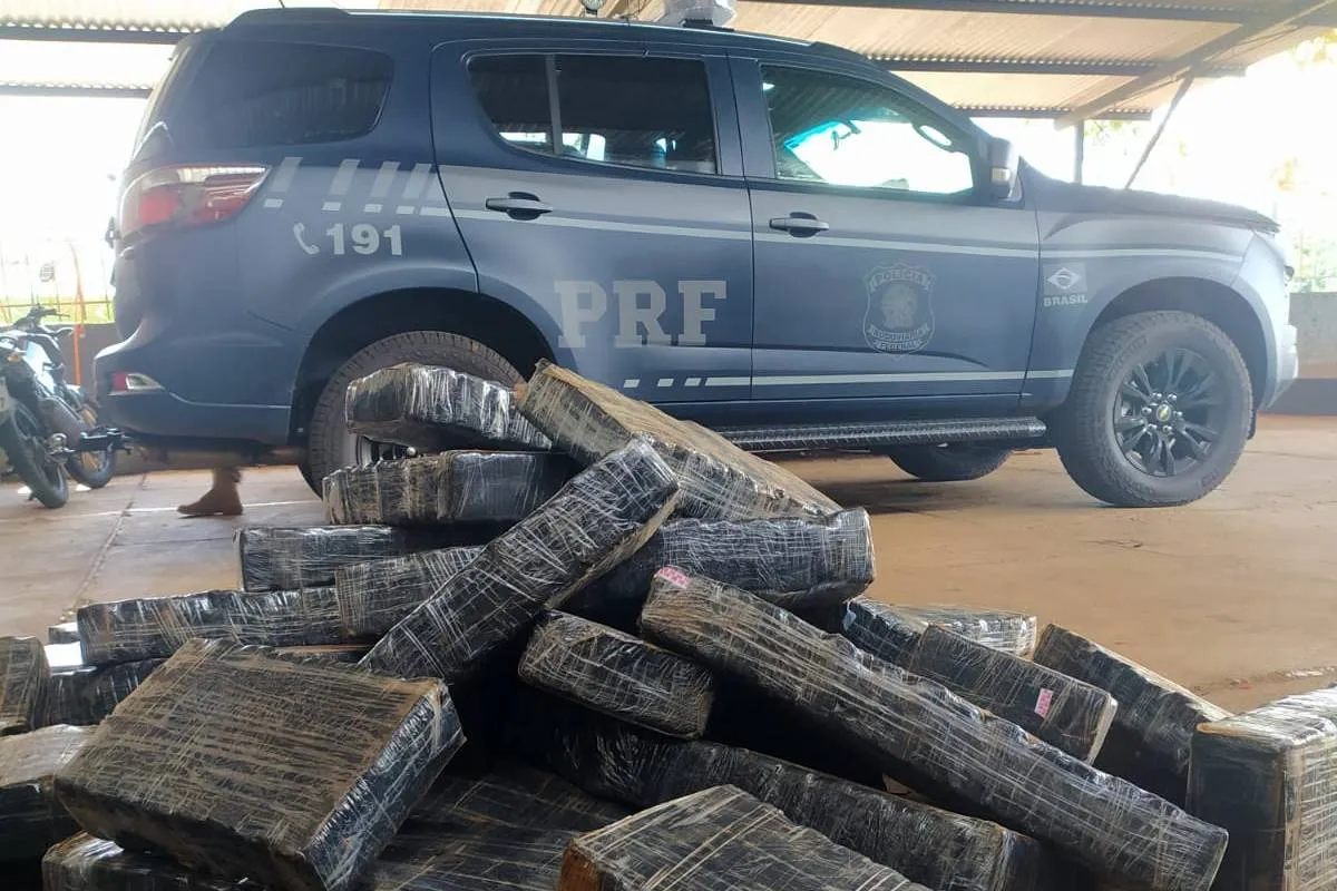 Imagem mostra uma viatura da PRF ao lado de pacotes de maconha.