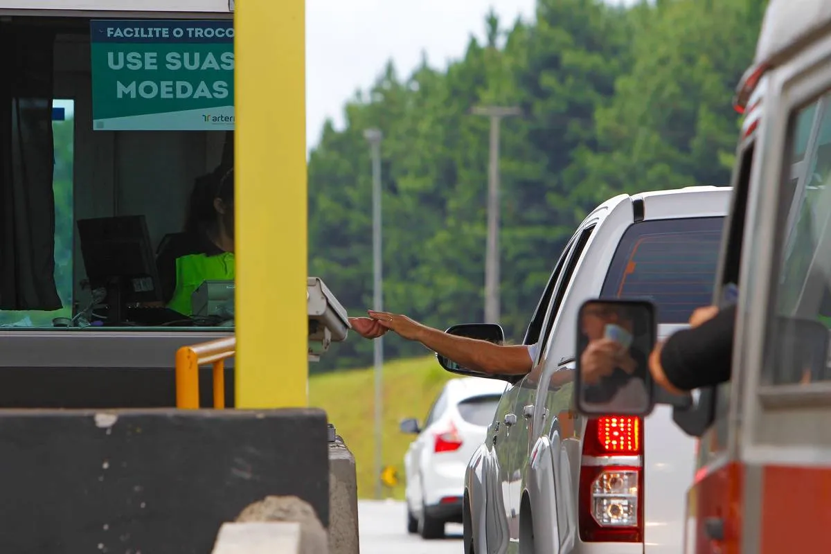 Imagem mostra uma praça de pedágio com motoristas pagando para passar