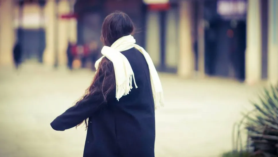 Imagem mostra uma mulher com muito frio, usando um cachecol e um sobretudo preto