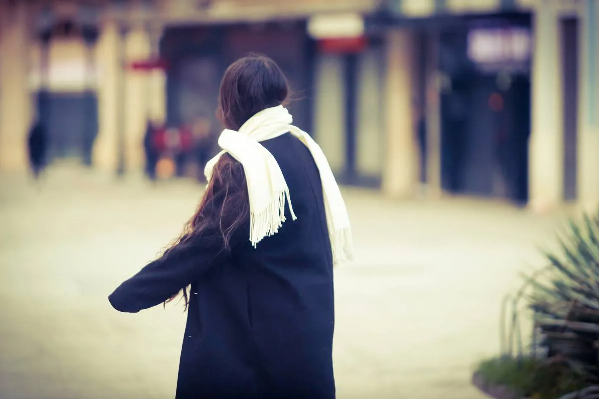 Imagem mostra uma mulher com muito frio, usando um cachecol e um sobretudo preto