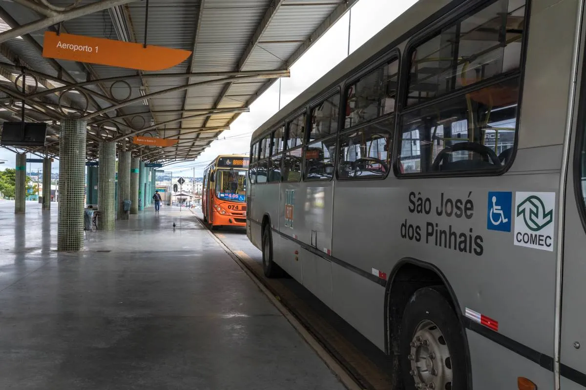 Imagem mostra um ônibus prata estacionado em um terminal.