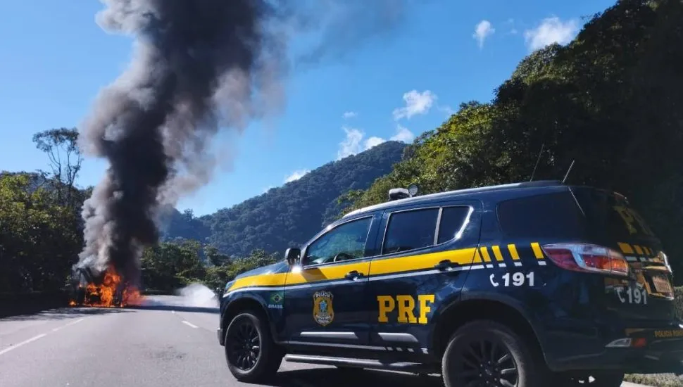 Imagem mostra um ônibus em chamas com uma viatura da PRF na escolta.