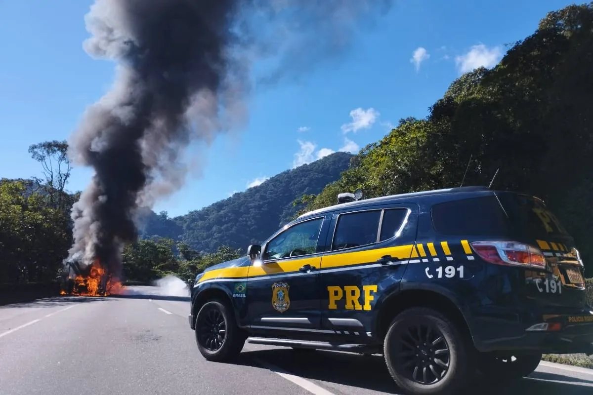 Imagem mostra um ônibus em chamas com uma viatura da PRF na escolta.