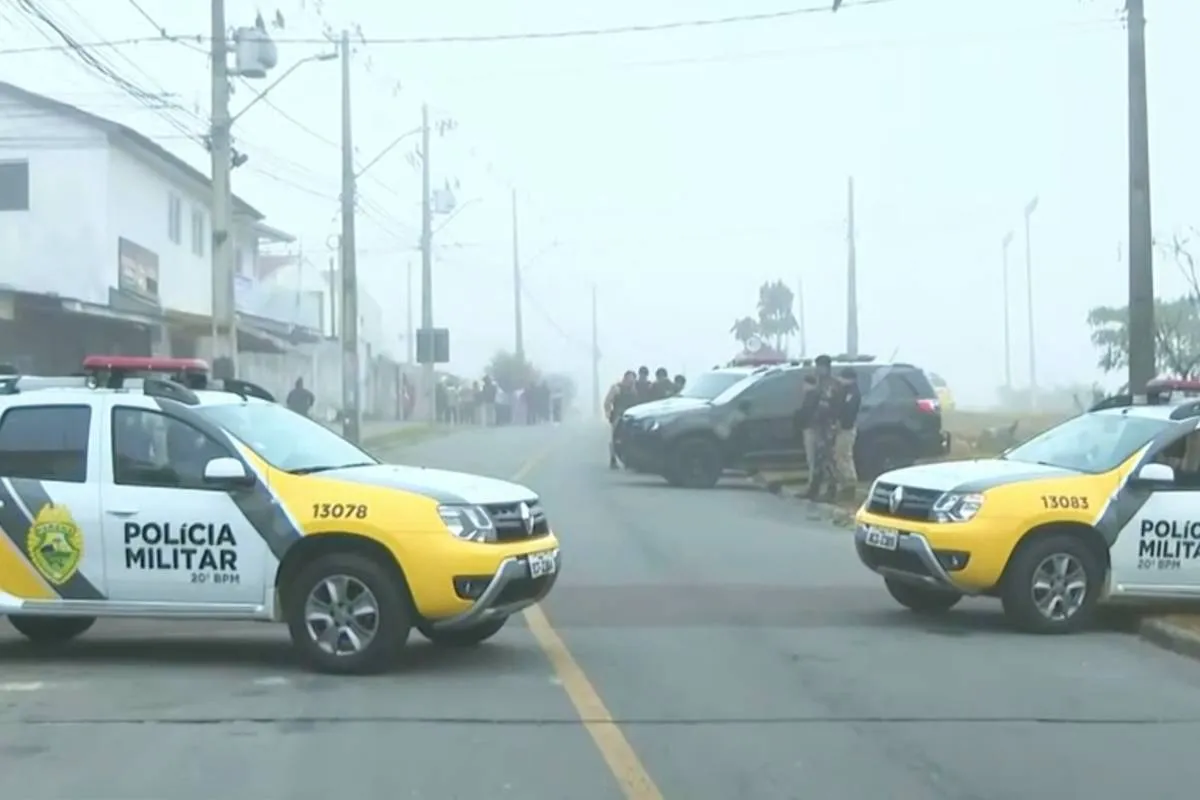 Imagem mostra três viaturas bloqueando uma rua em Curitiba. Há neblina na pista.