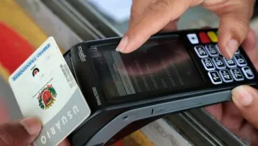 Imagem mostra uma pessoa recarregando um cartão transporte numa maquininha