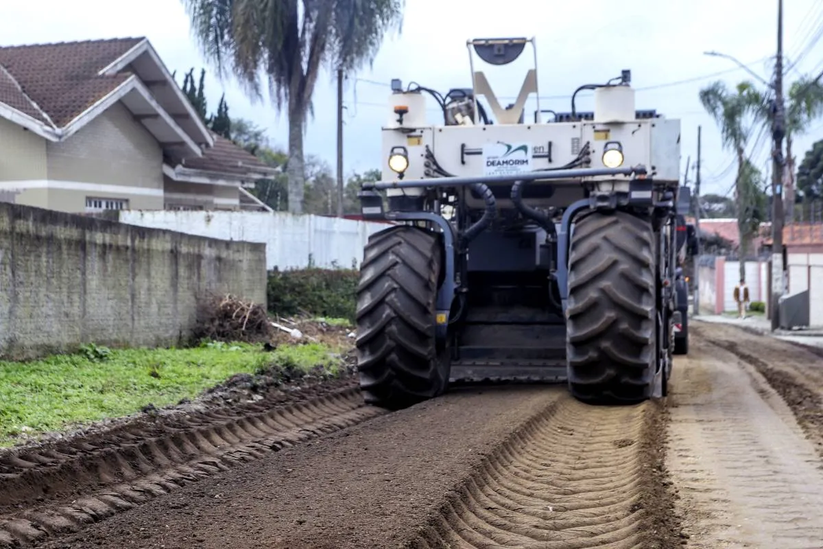 Imagem mostra uma máquina gigante trabalhando em uma rua sem asfalto