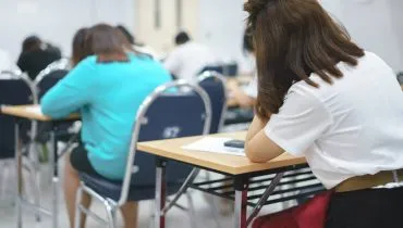 Imagem mostra pessoas fazendo uma prova em uma sala de aula.
