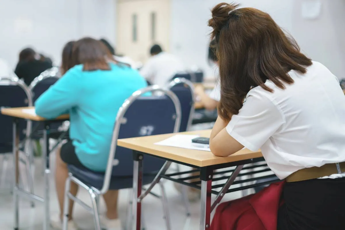Imagem mostra pessoas fazendo uma prova em uma sala de aula.