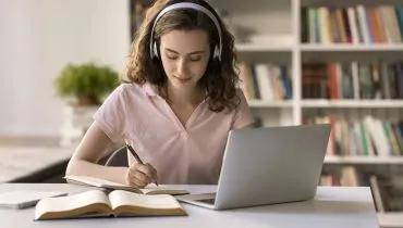 Imagem mostra mulher escrevendo em caderno e usando notebook