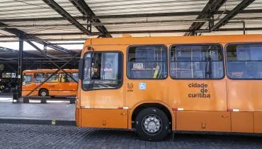 Imagem mostra 2 ônibus parados em pontos de um terminal em Curitiba