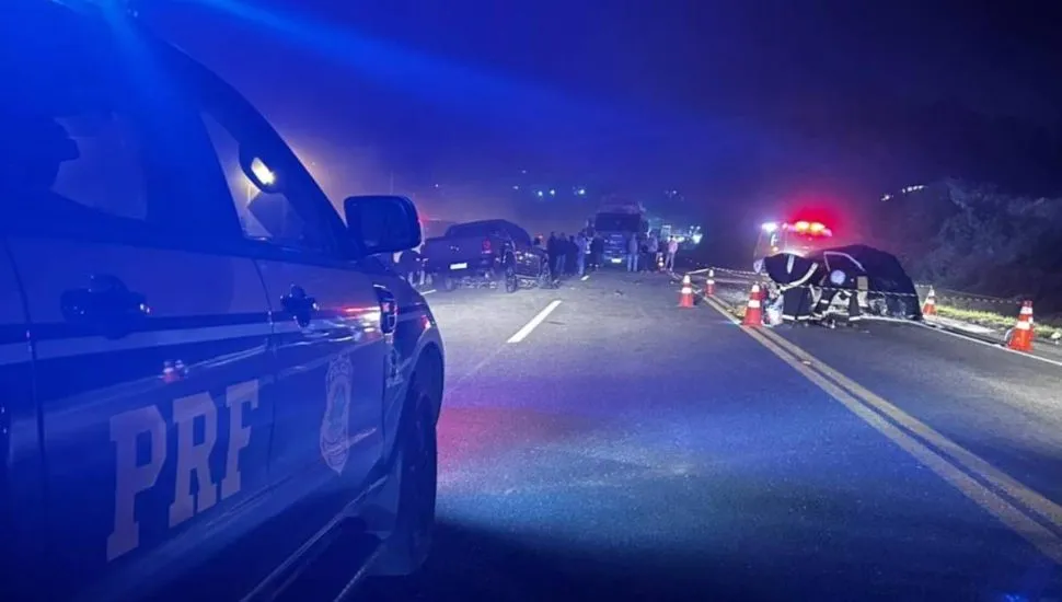 Imagem mostra um acidente na BR-476. Tem um carro da PRF e uma iluminação azul por causa do giroflex da viatura. Ao fundo, um carro destruído.